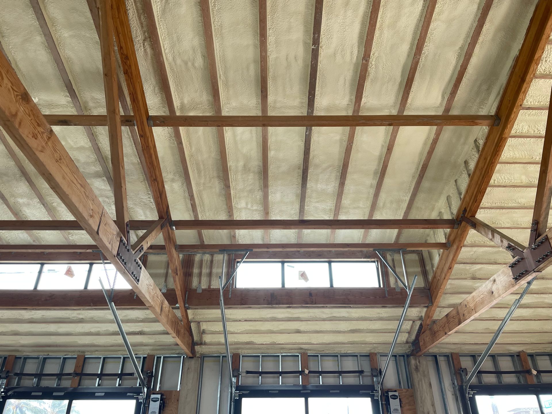 Interior view of a building's ceiling insulated with foam, wood beams, and a row of windows.