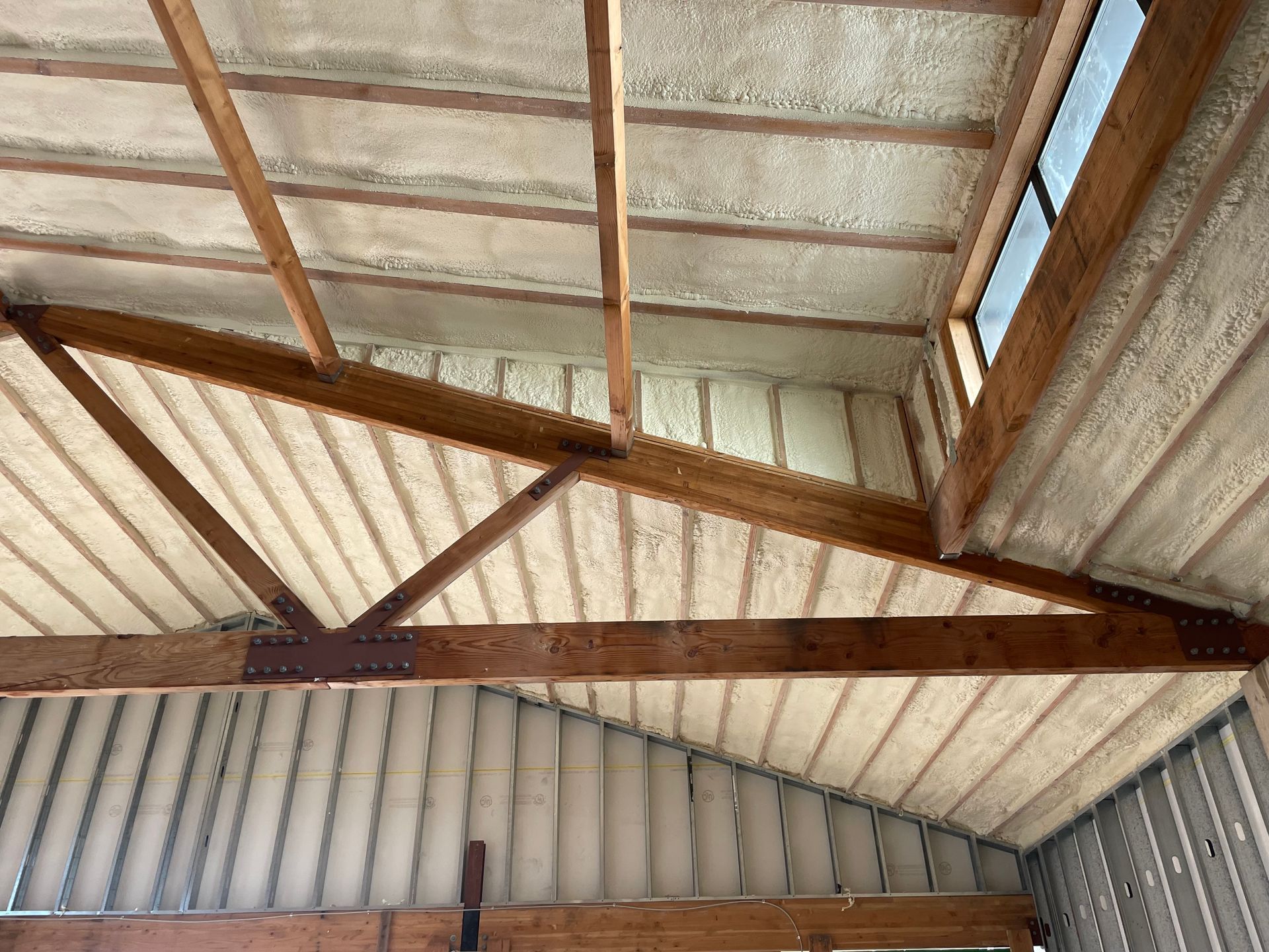 Interior view of a building roof with spray foam insulation between wooden beams and walls.