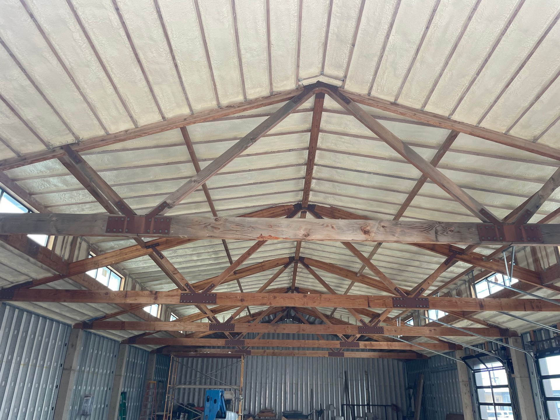 Wooden rafters and trusses supporting an interior ceiling with a corrugated metal wall in background.