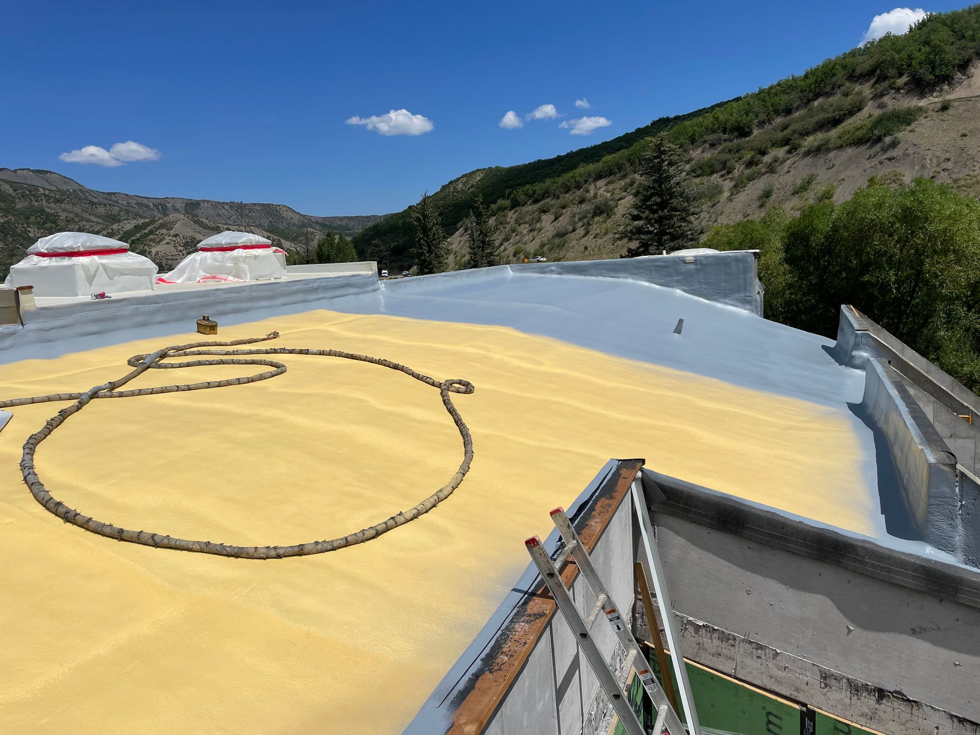 A partially sprayed yellow roof with mountains and blue sky in the background.