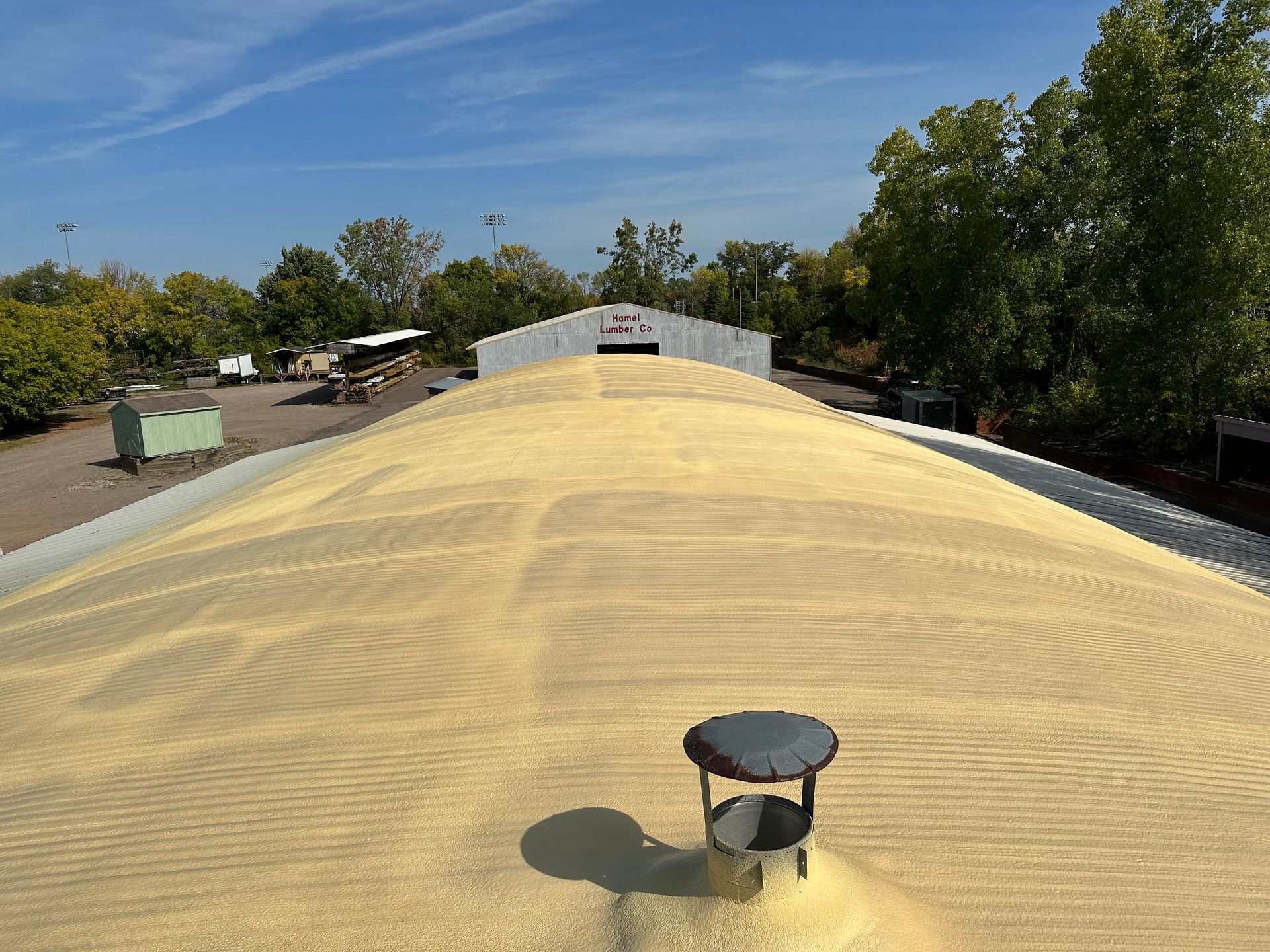 Pile of grain on a roof with a vent and a blue sky.