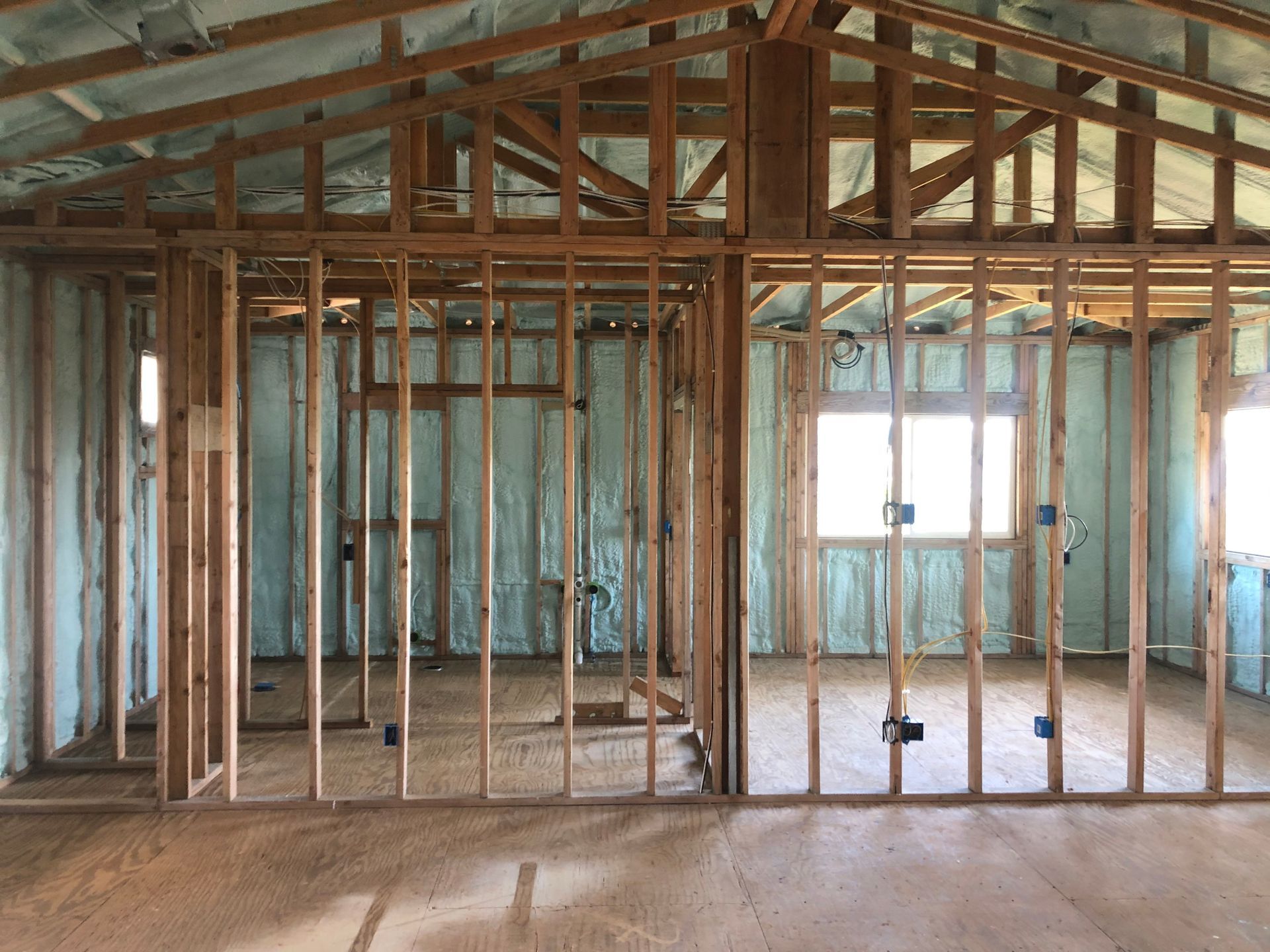 Interior framing of a building under construction, walls sprayed with light blue insulation.
