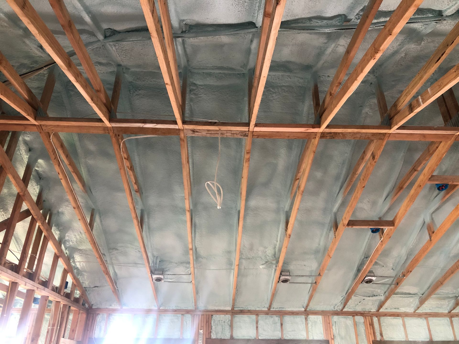 Unfinished ceiling with exposed wooden beams, insulation sprayed between them.