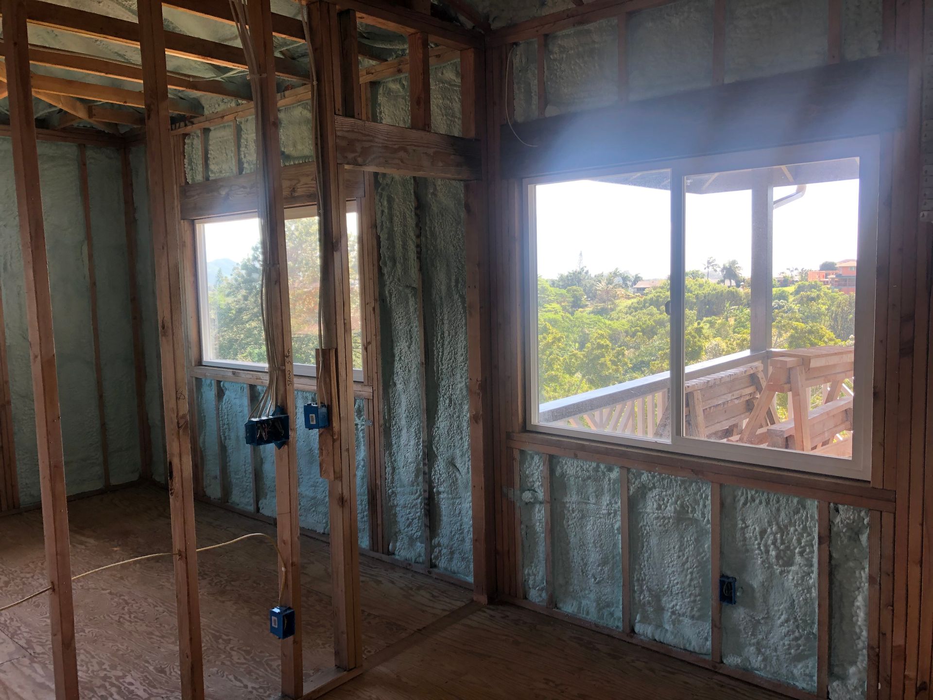 Interior of a room under construction, spray foam insulation on walls, framed windows, wooden structure.