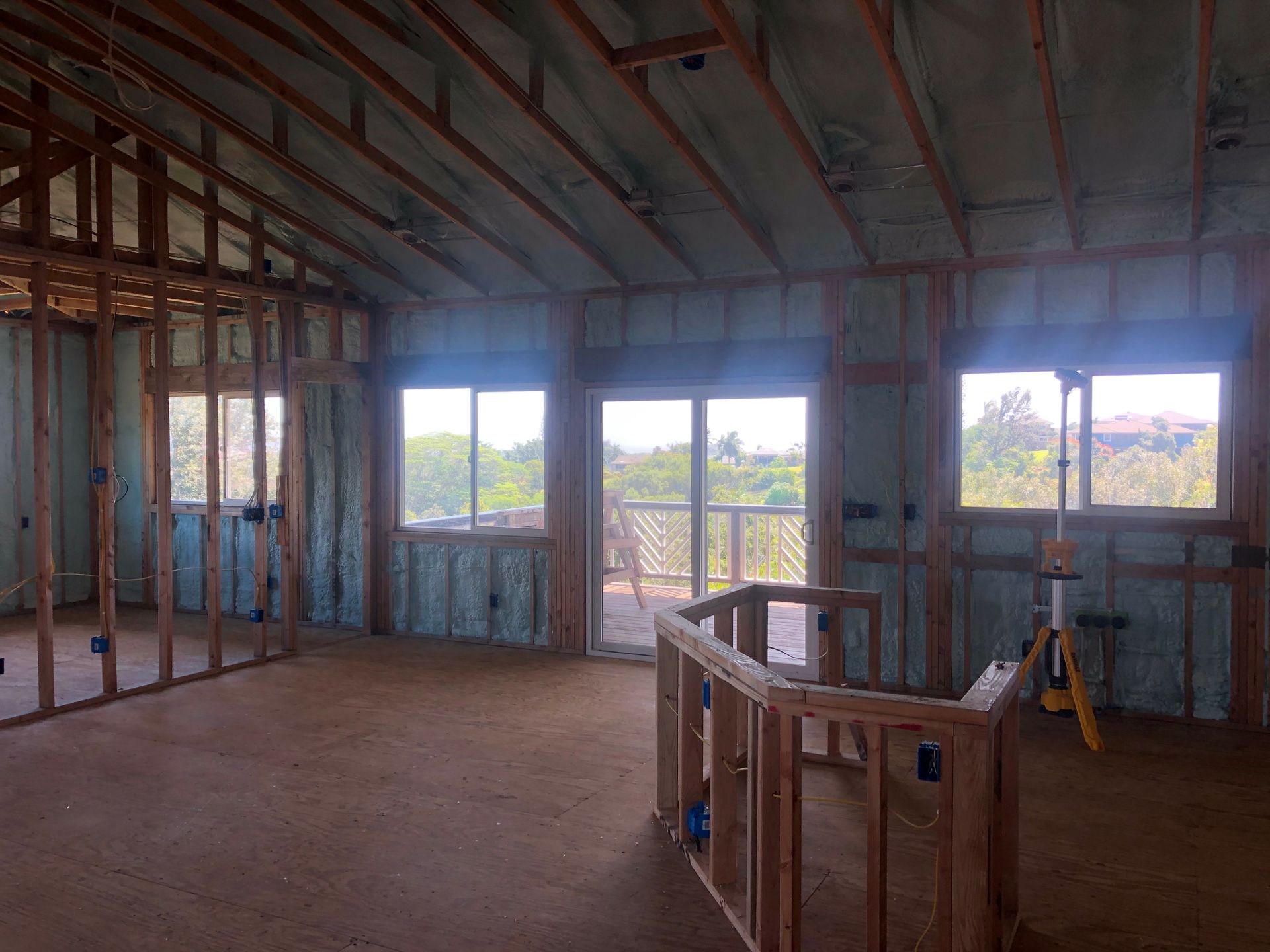 Interior of a room under construction, with wooden frame, spray foam insulation, and windows overlooking a deck.