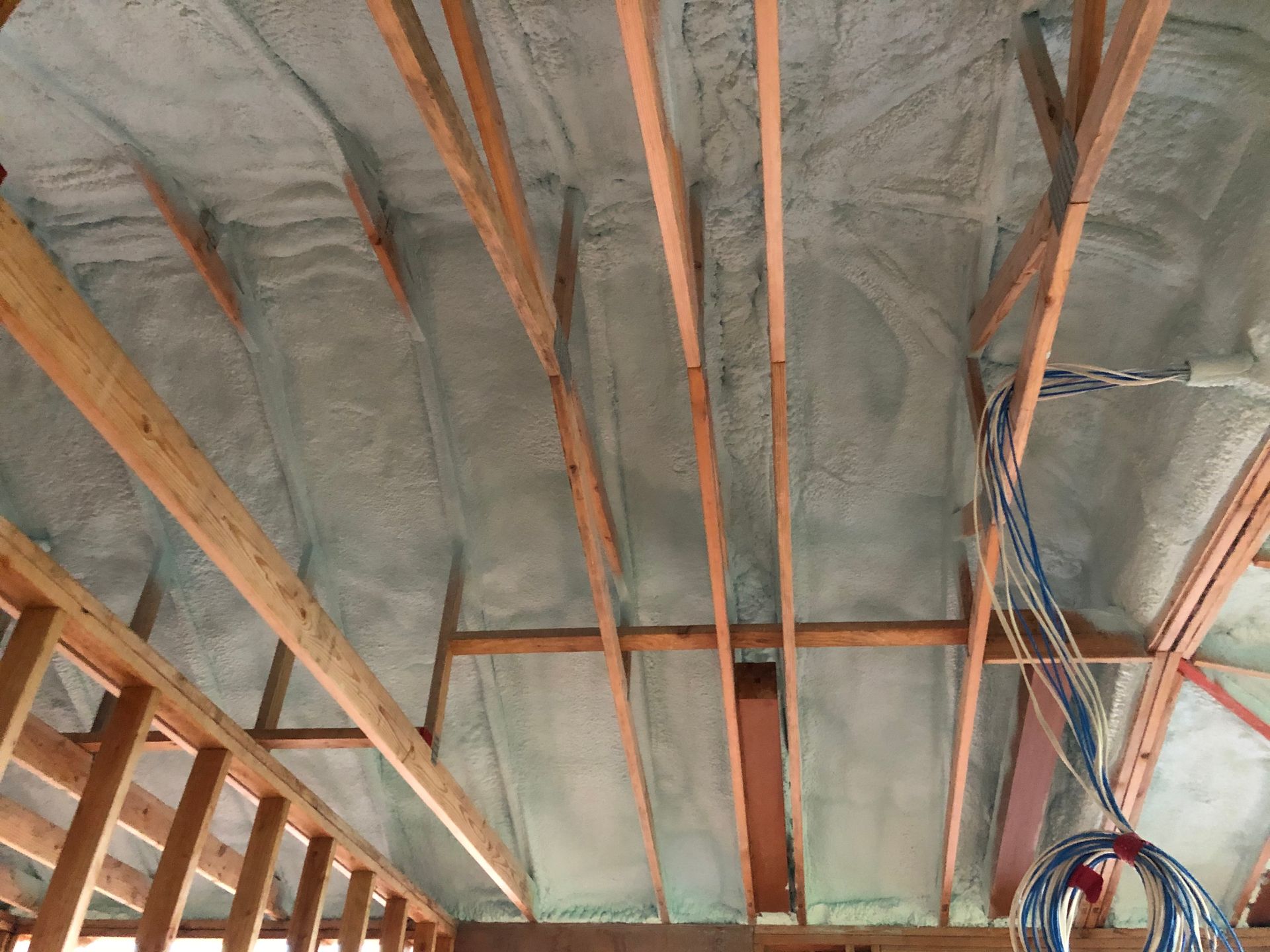 Wooden rafters covered with gray spray foam insulation in a construction setting.
