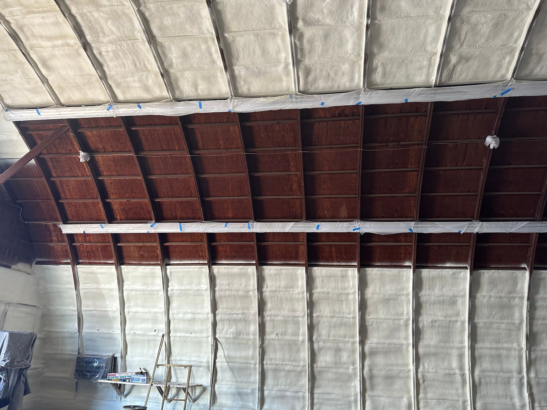 Interior view of a building's ceiling and wall with brown wood and white foam insulation.
