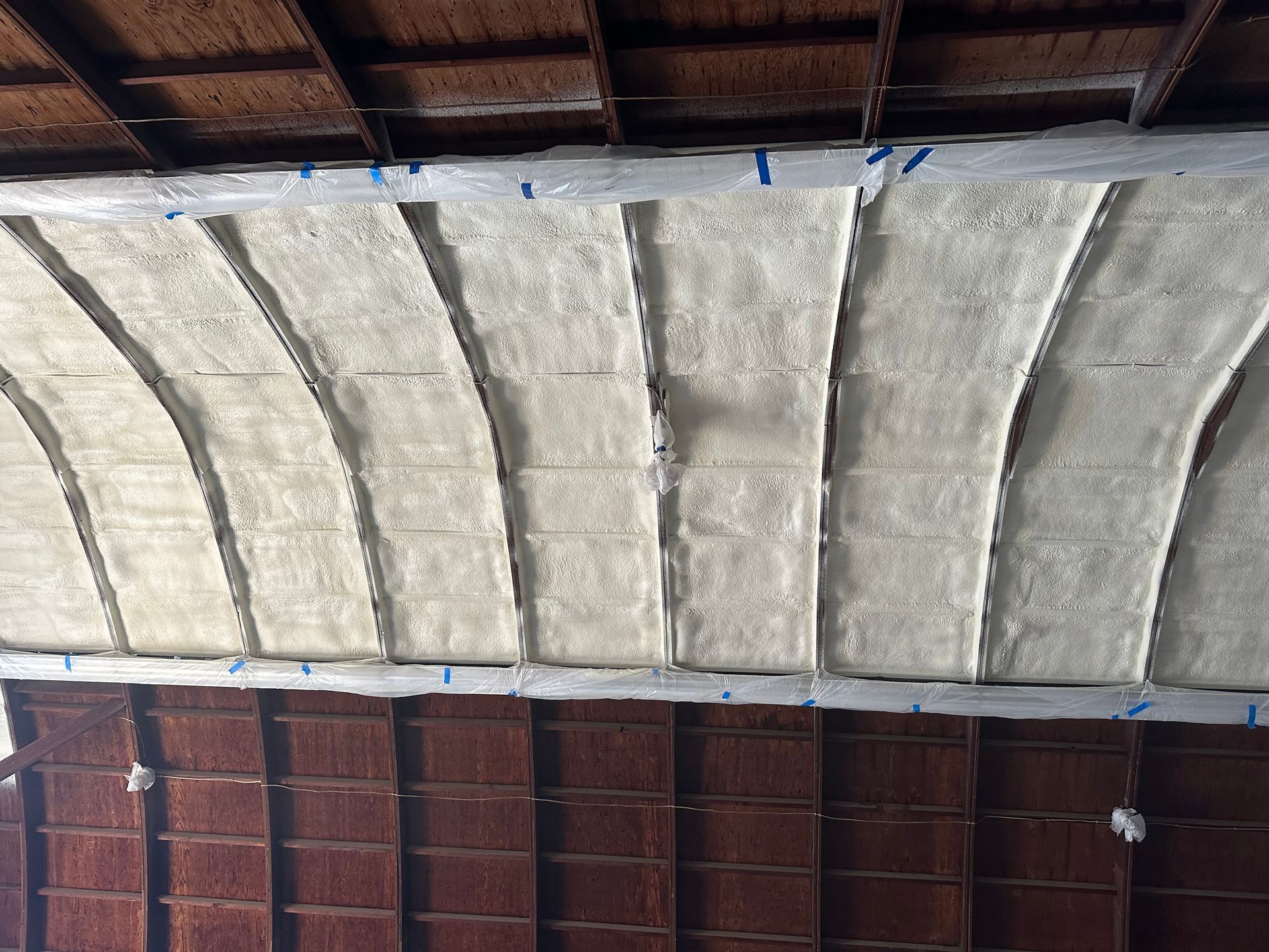 Insulation installed in an arched ceiling, white and gray against a dark wood ceiling and wall.