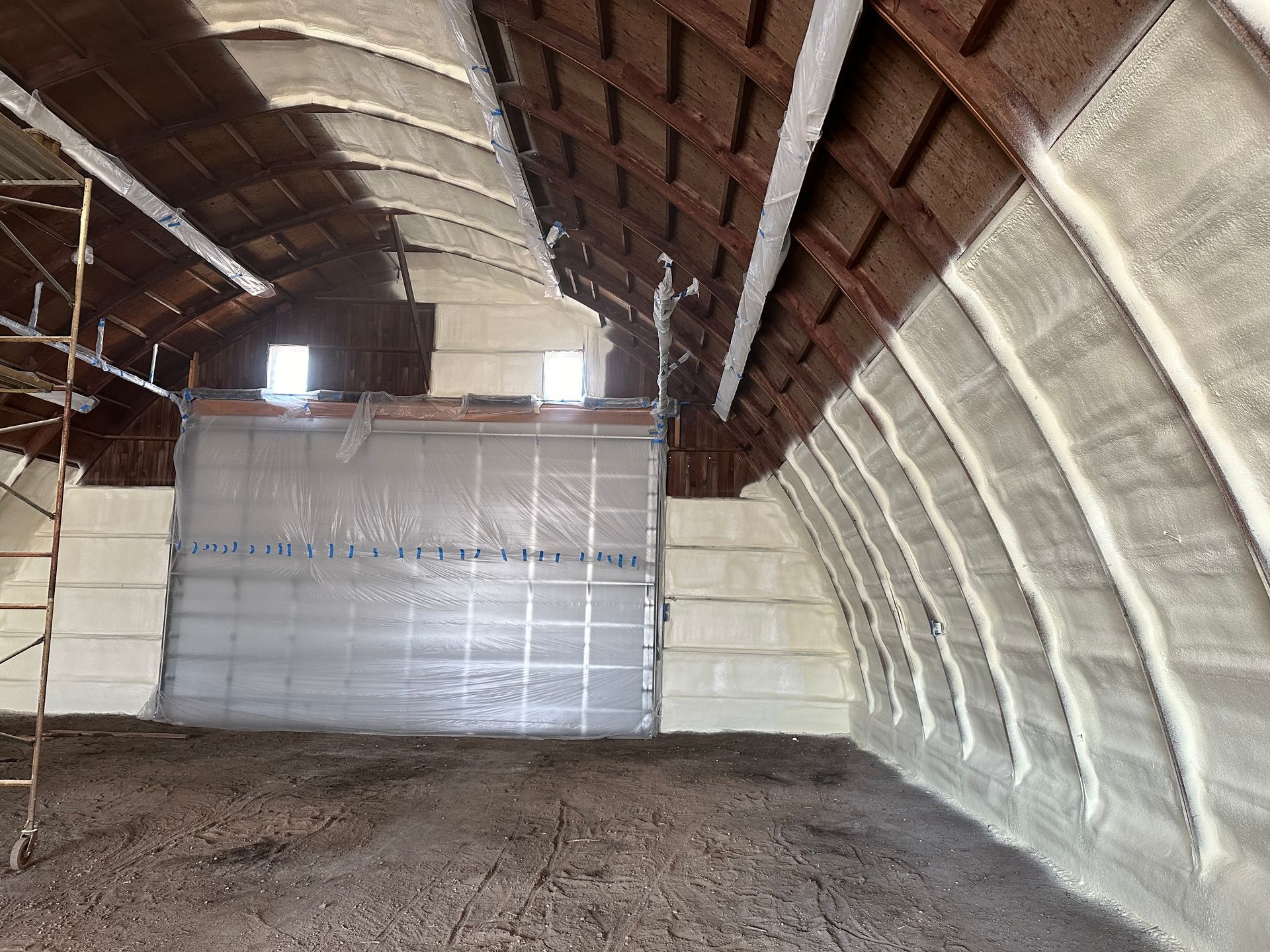 Interior of a building being insulated with spray foam; curved wood ceiling and walls. Beige foam is applied.