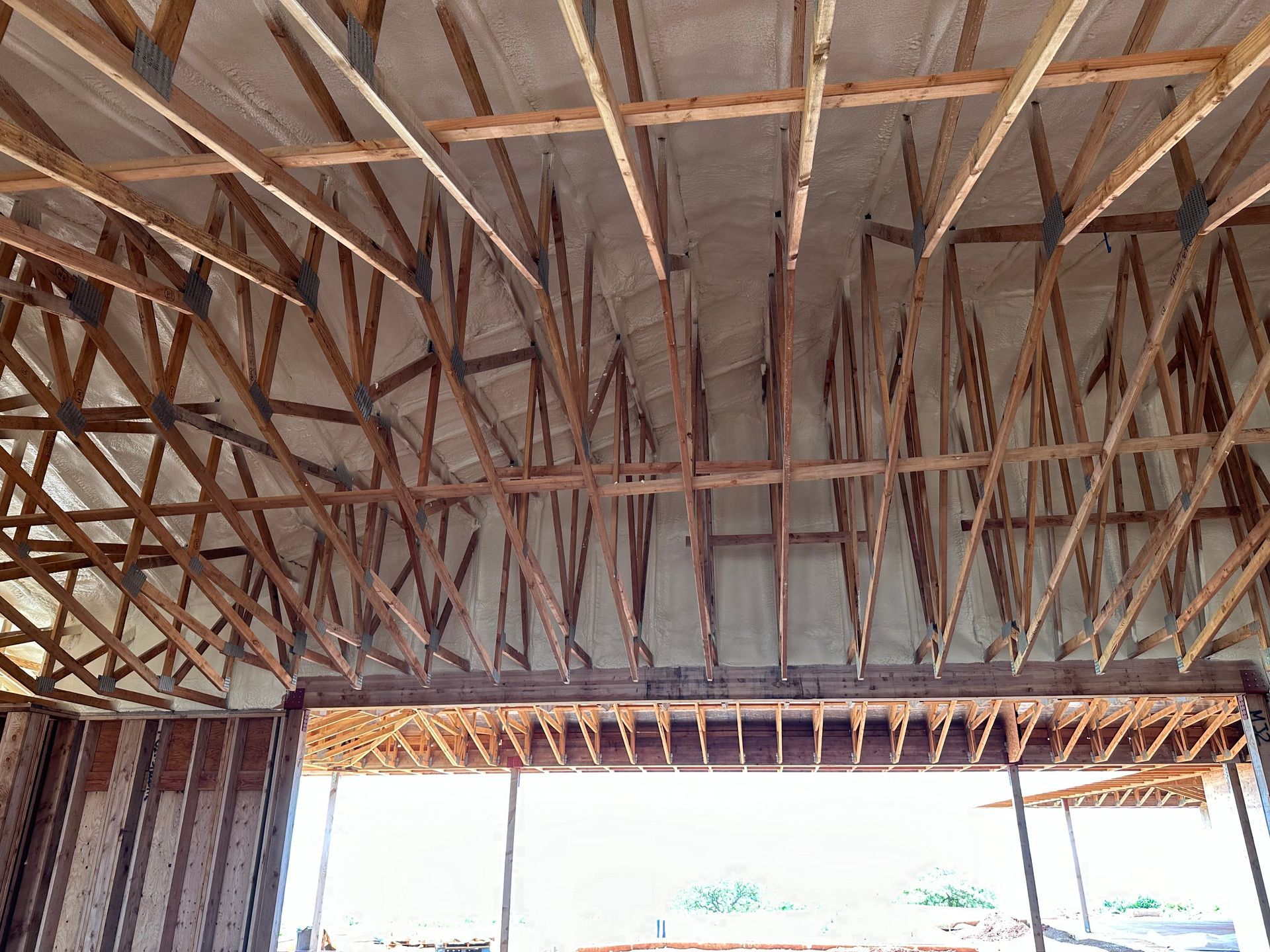 Wooden roof trusses and framing of a building's interior, showing insulation.