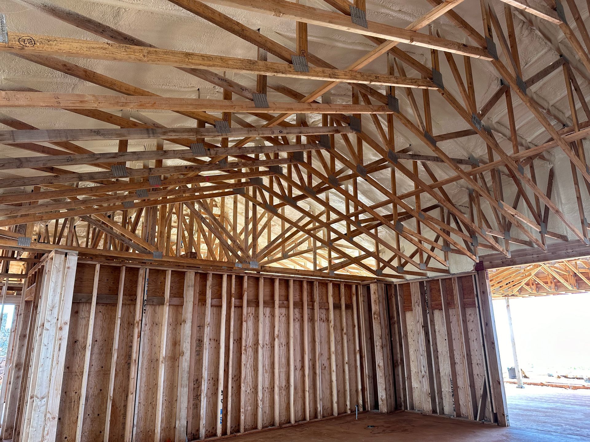 Interior view of a building under construction, showing wooden framing, roof trusses, and insulation.