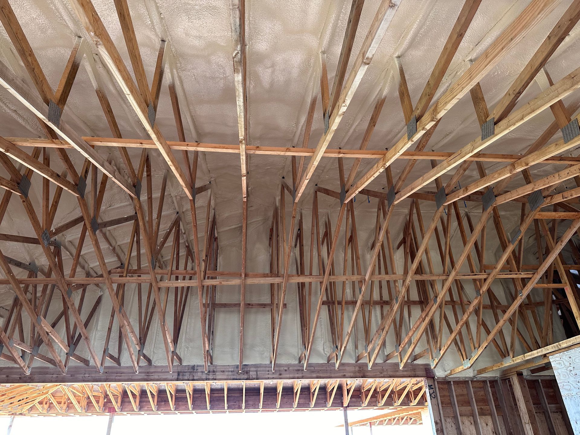 Wooden rafters of a building's roof with insulation sprayed between the beams.