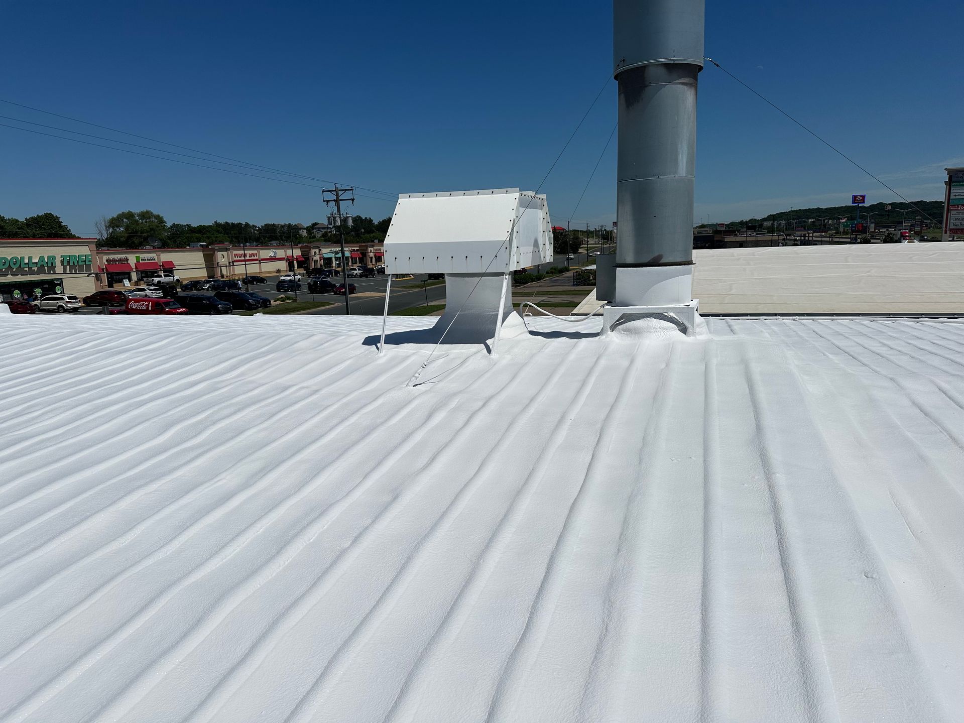 White-coated corrugated metal roof with vent pipes and a sunny, clear sky in the background.