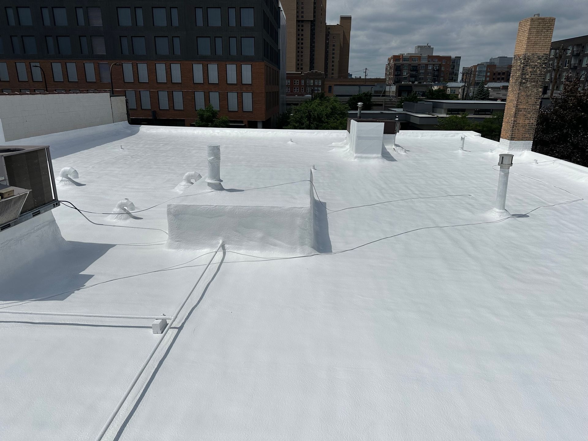 White-coated rooftop with various vents, pipes, and city buildings in the background.