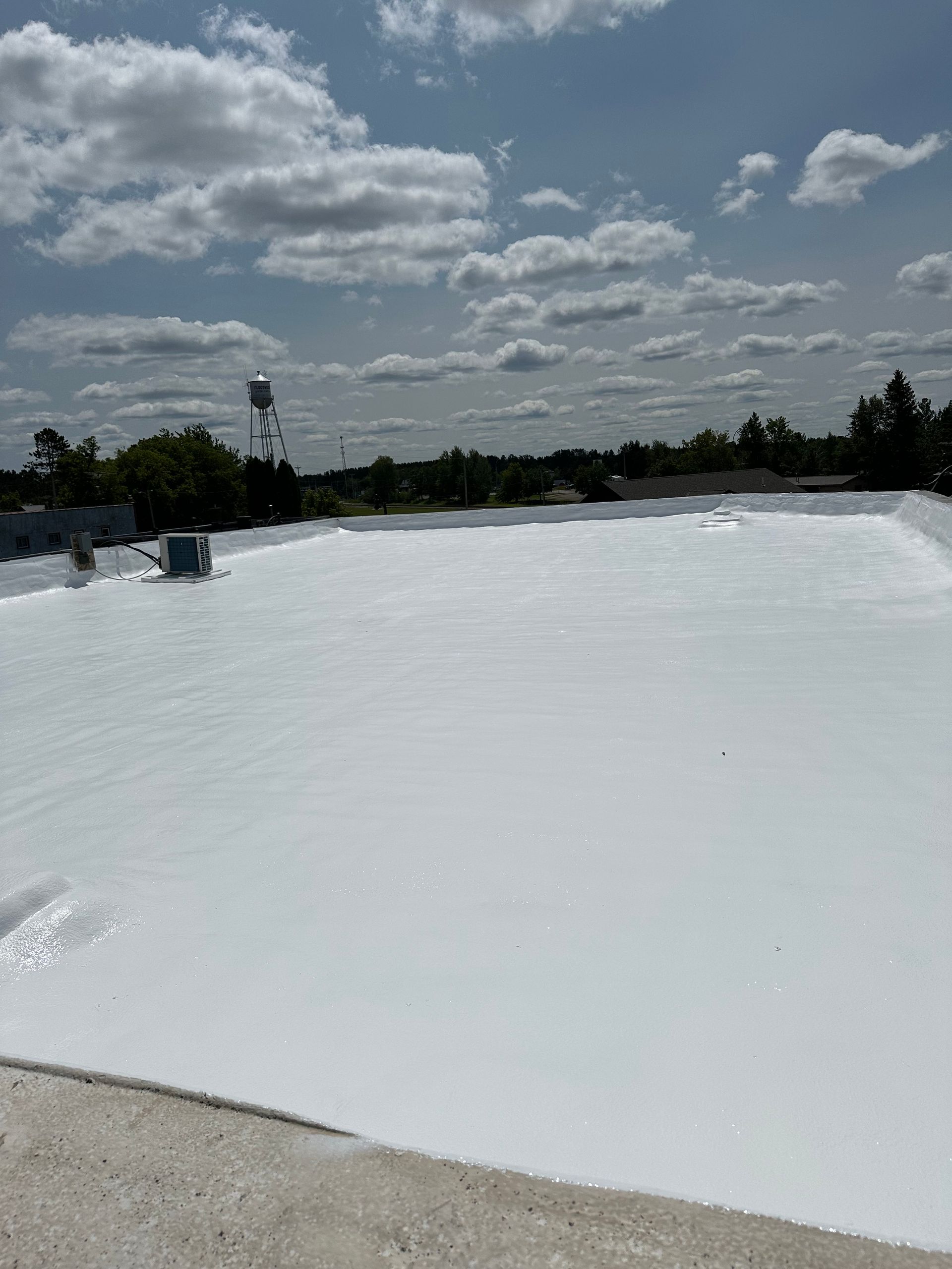 White-coated flat roof under a partly cloudy blue sky, with trees visible in the distance.