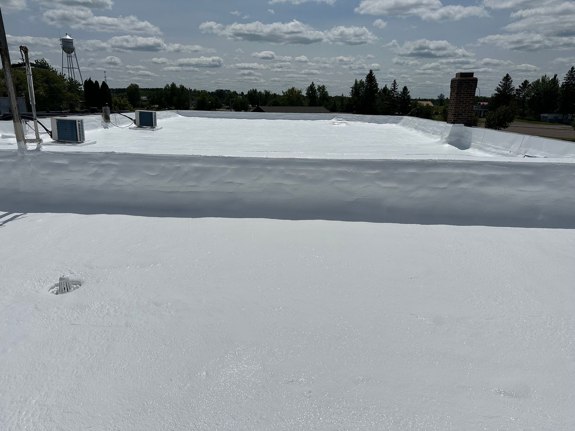 White-coated commercial rooftop with sky, trees and some equipment.