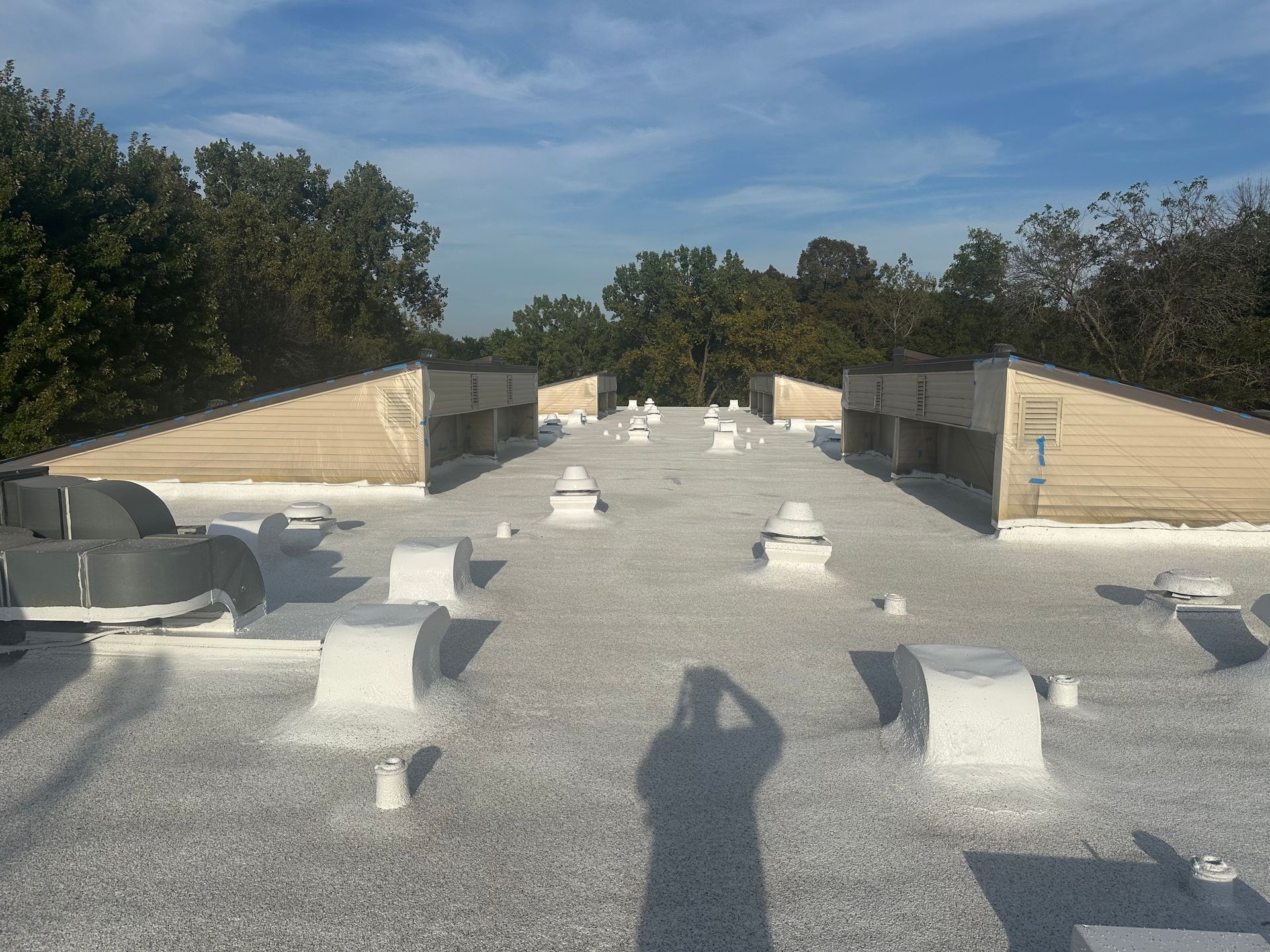A low-angle shot of a flat commercial roof with multiple vents and surrounding trees under a blue sky.