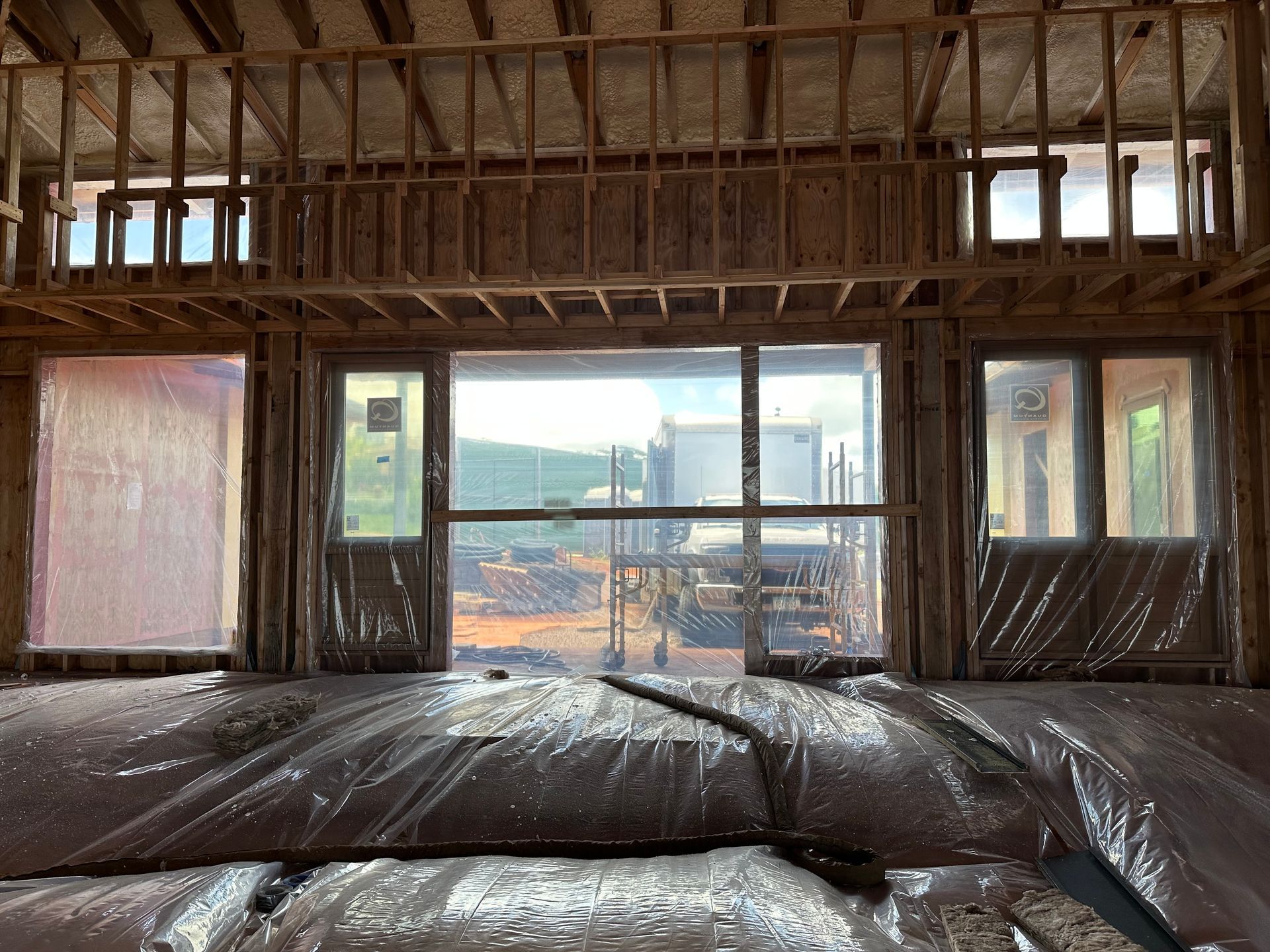 Interior of a building under construction, showing wooden frame, windows, and plastic sheeting.