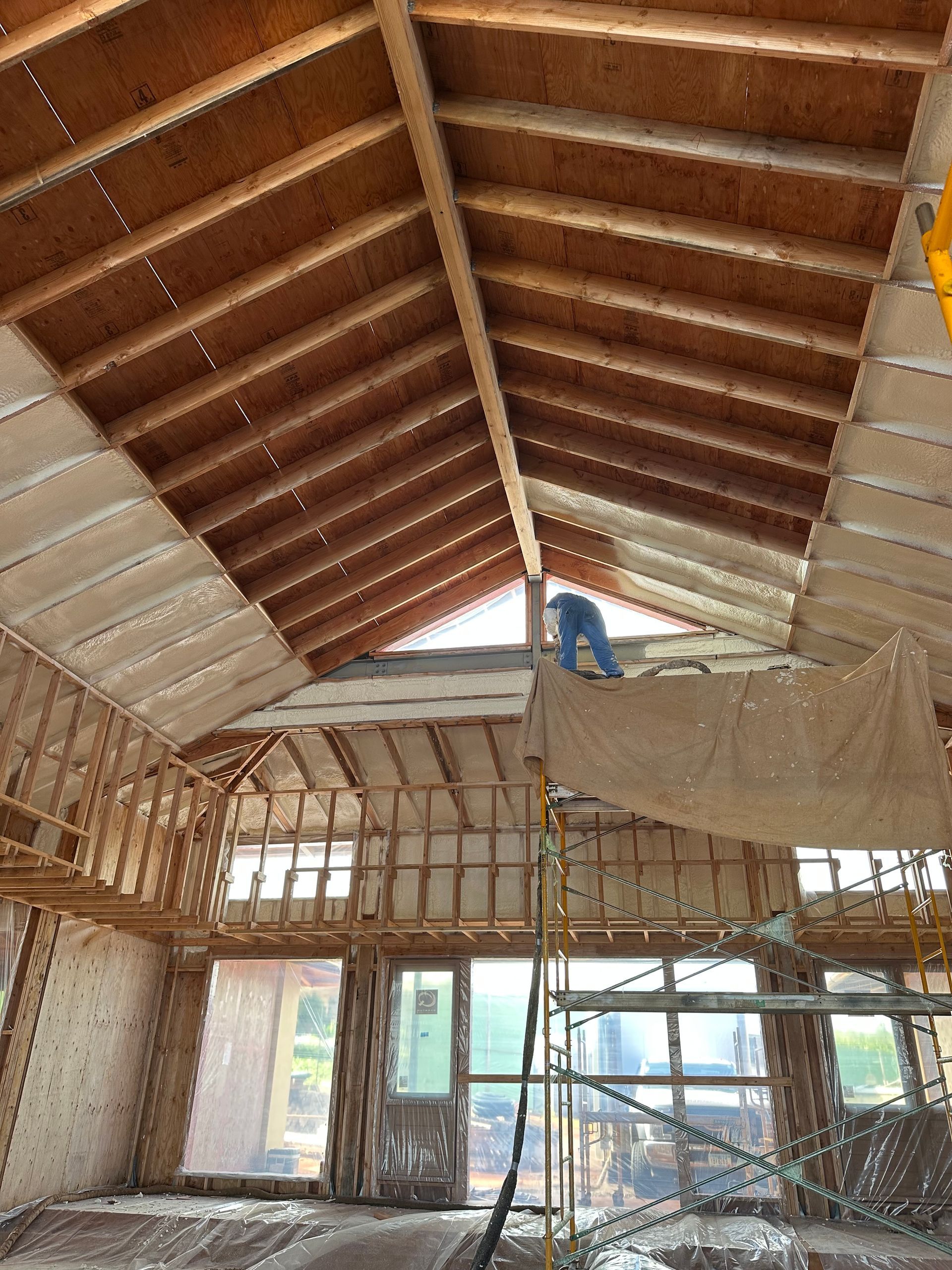 Interior of a building under construction, showing wooden rafters, insulation, and a person working on a high platform.
