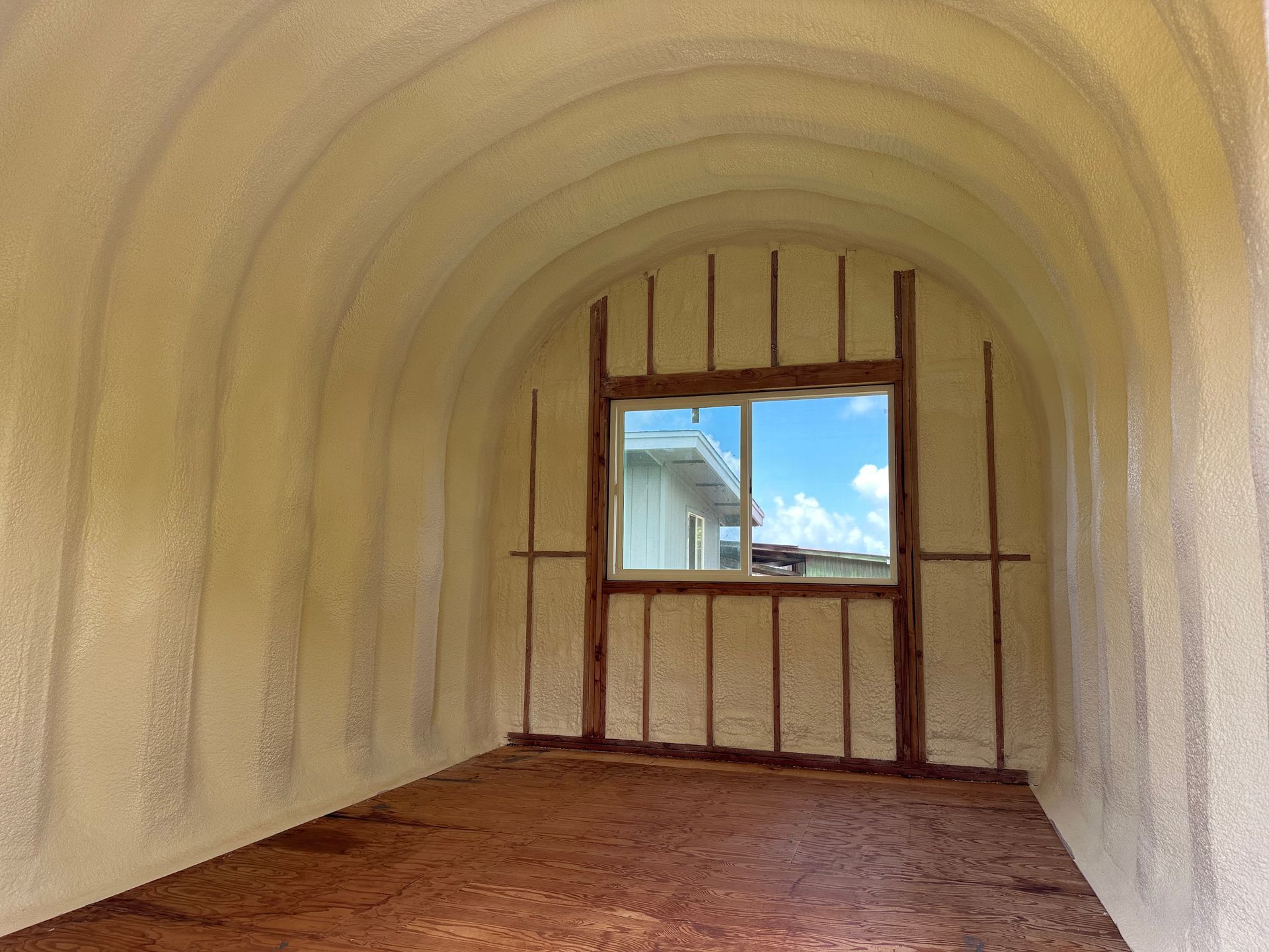 Interior view of arched-roof structure with spray foam insulation, a window, and wood framing.