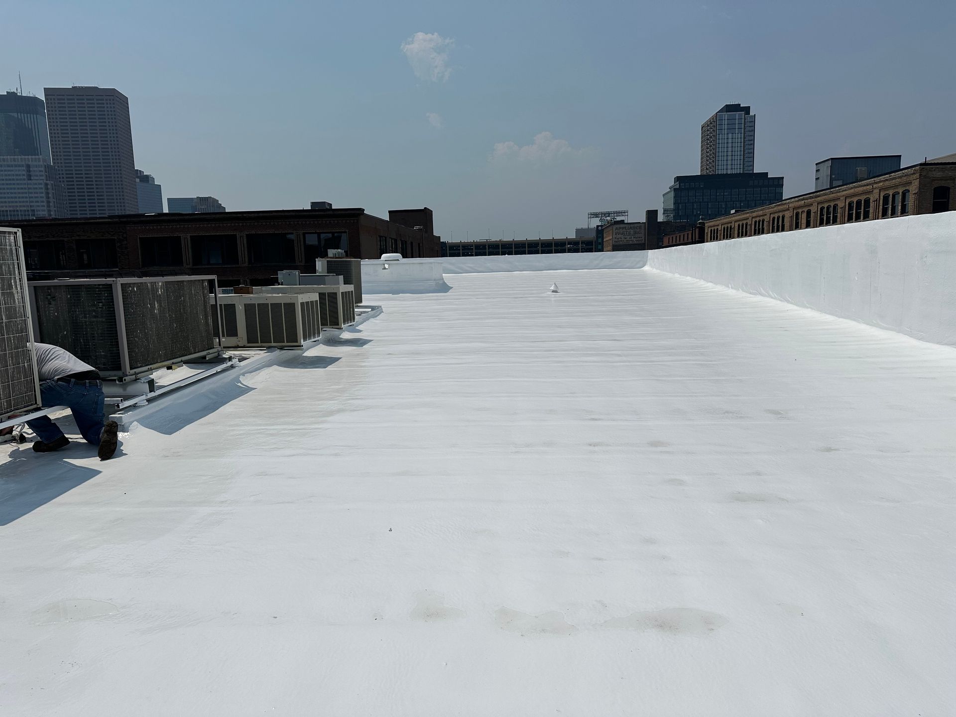 White flat rooftop with city skyline in the background. Someone works near the edge.