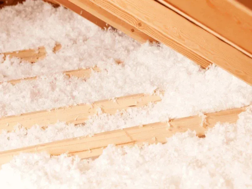White insulation fills the space between wooden rafters in an attic.