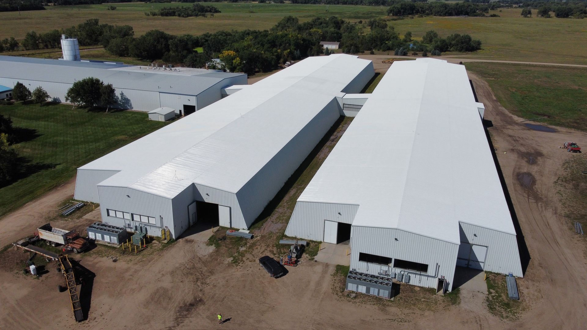 Aerial view of two long white industrial buildings on a dirt lot.