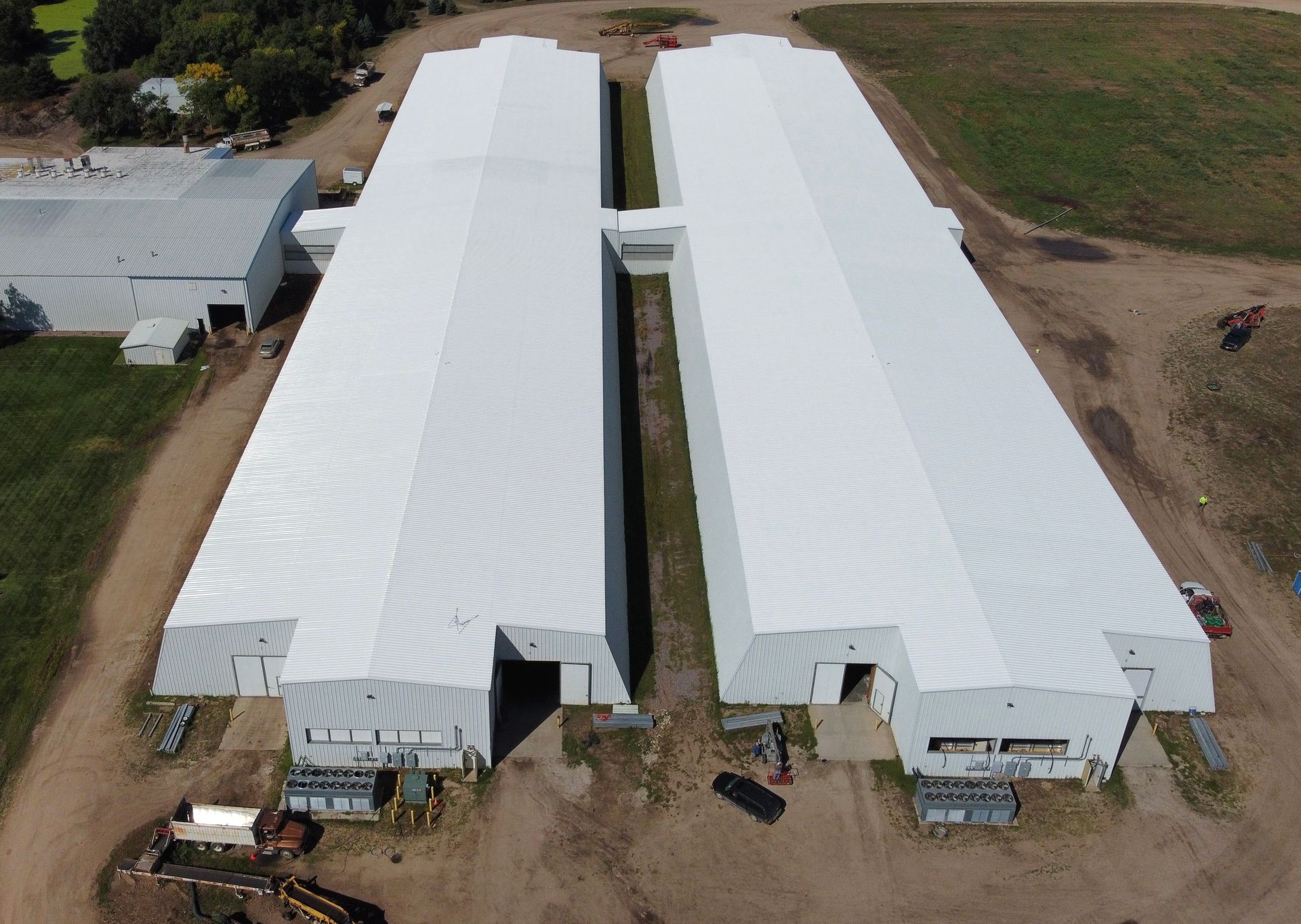 Two large white industrial buildings with visible entryways on a dirt lot.