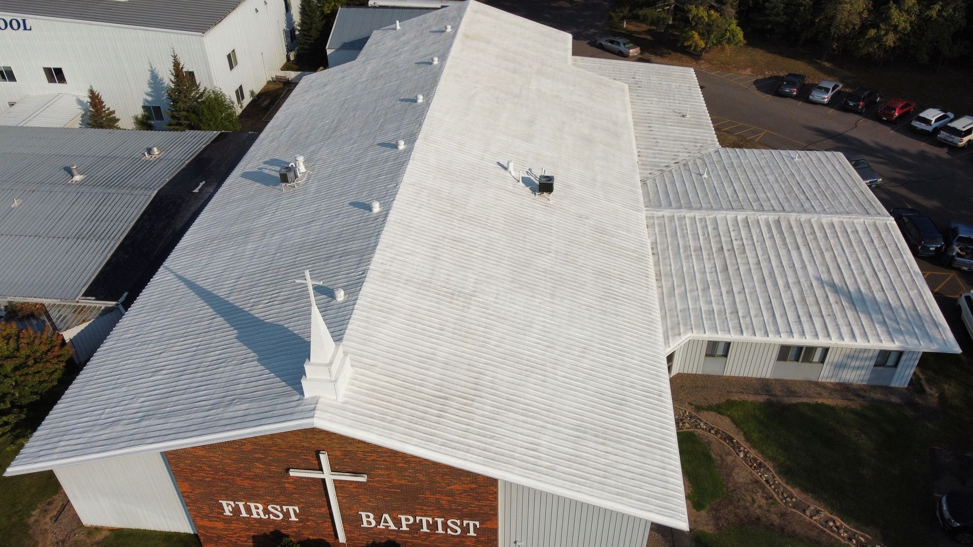 Aerial view of a white-roofed First Baptist church with a steeple and cross.