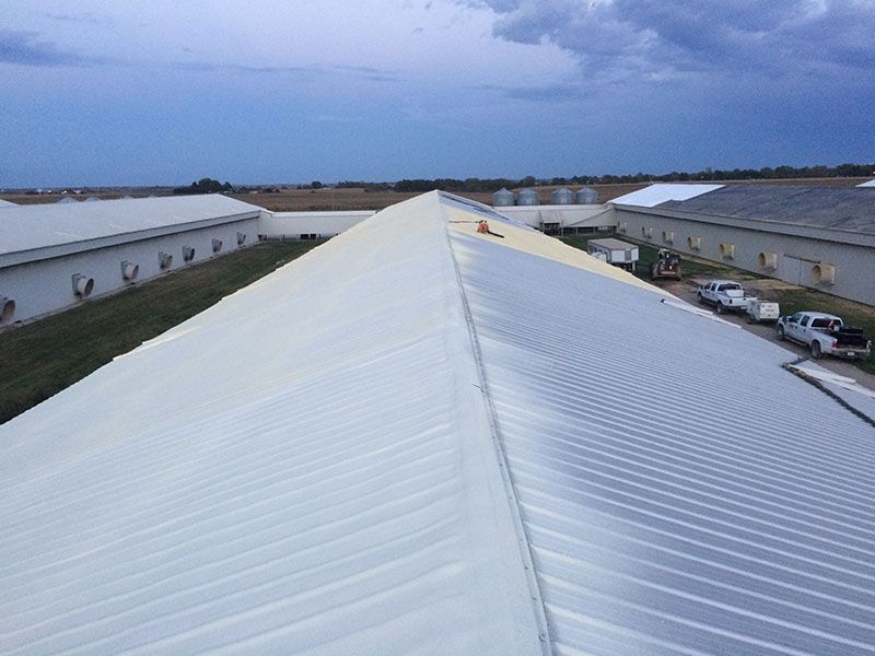 White industrial building roofs, partially painted, with a cloudy sky.