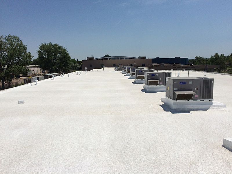 White commercial roof with air conditioning units; building in the background on a sunny day.