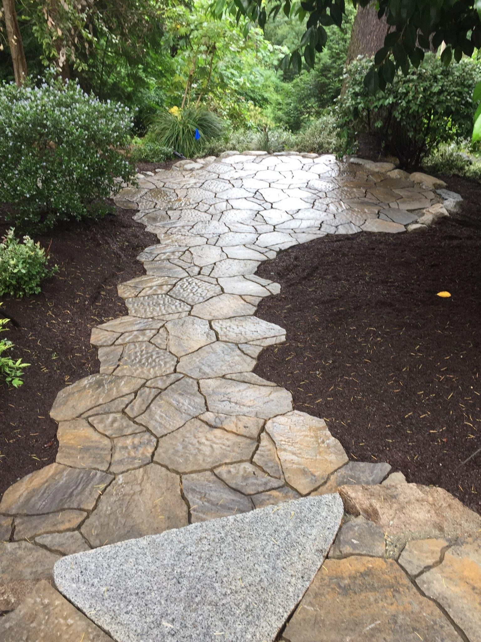 A stone walkway in a garden surrounded by trees and bushes in Monroe, WA.