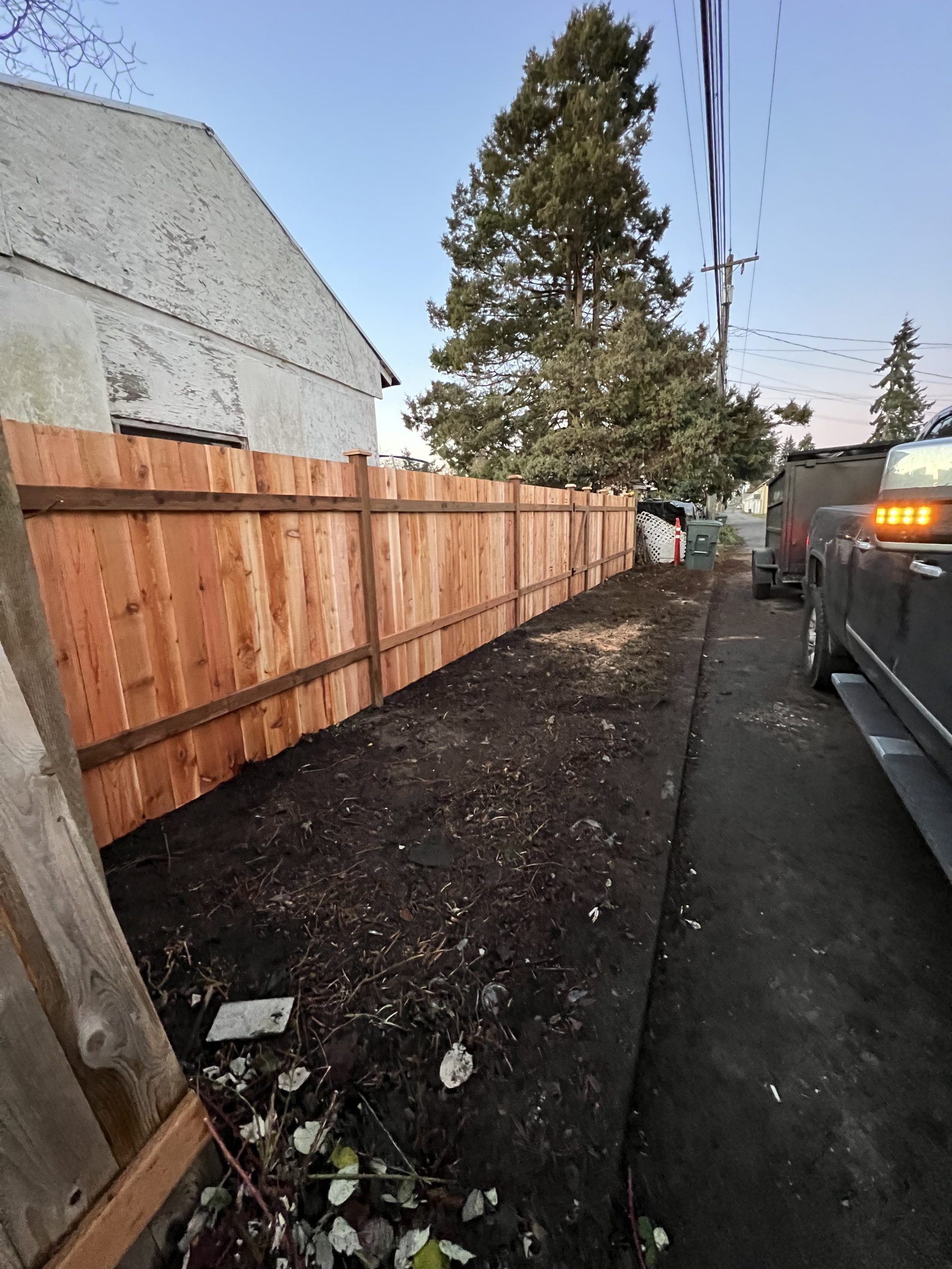 A wooden fence is sitting on the side of the road next to a house in Monroe, WA.