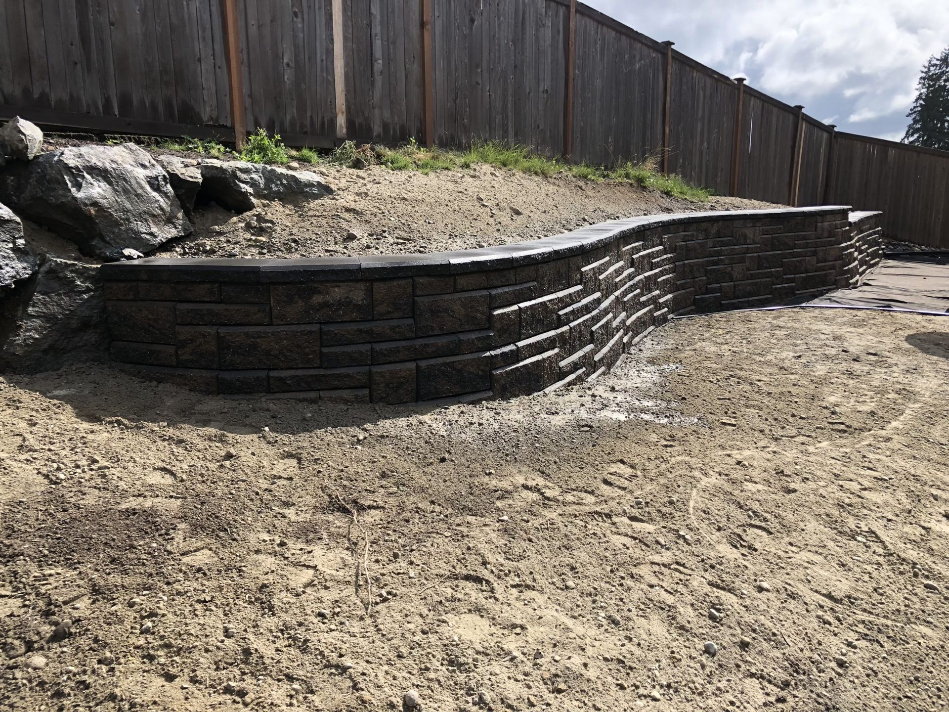 A brick wall is sitting in the middle of a dirt field next to a wooden fence in Monroe, WA.