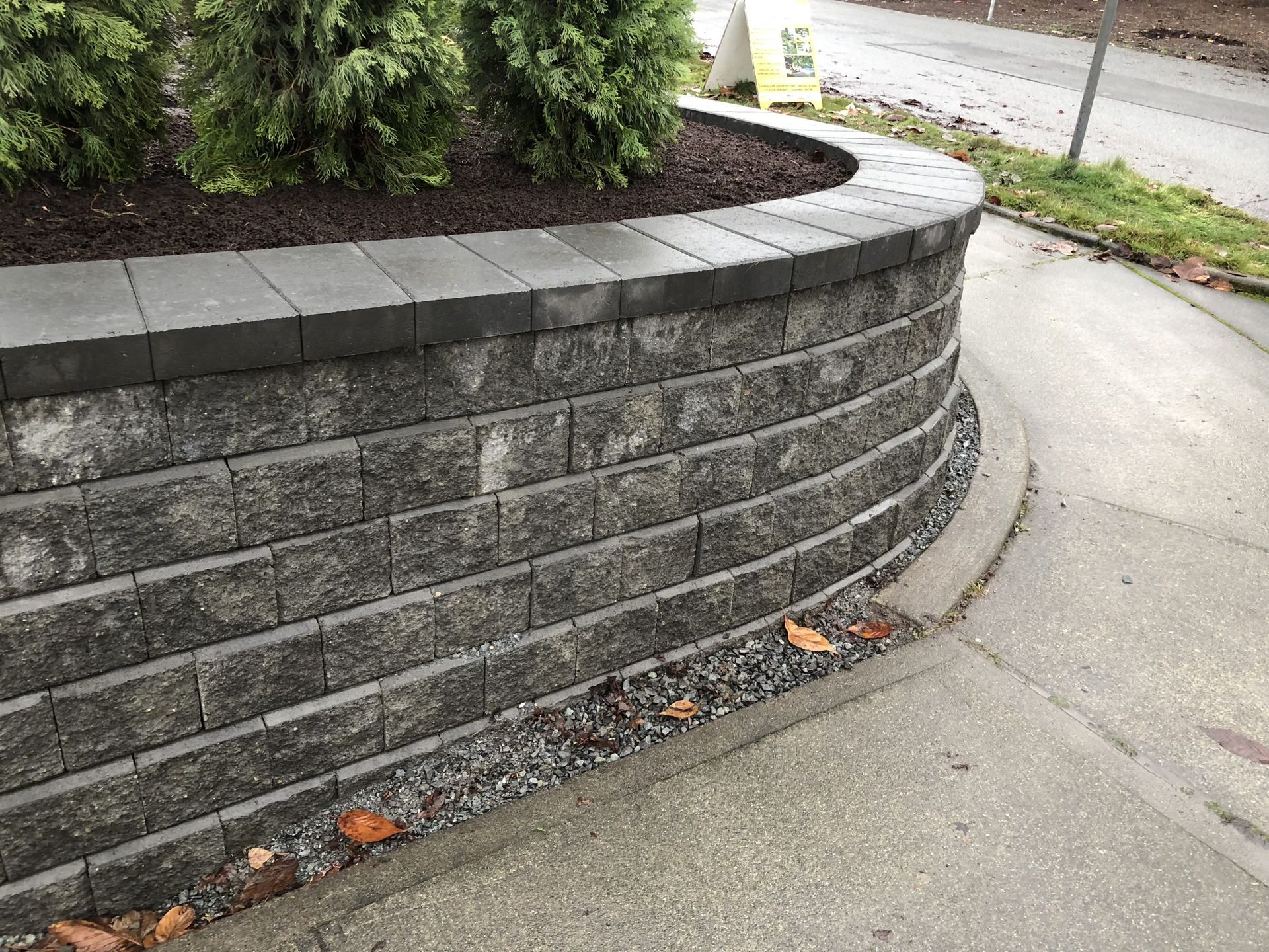 A brick wall with a planter on top of it next to a sidewalk in Monroe, WA.