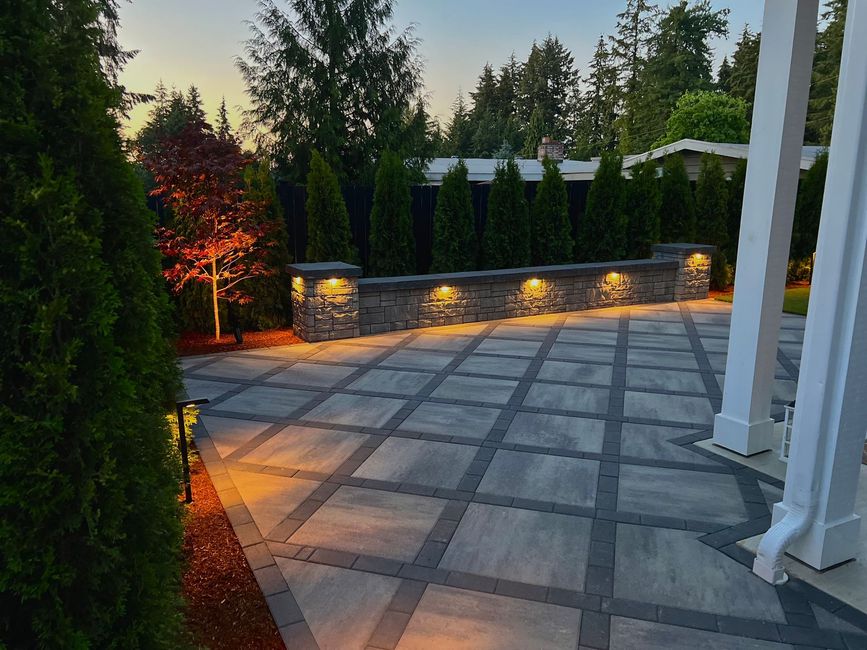 A patio with a stone wall and trees is lit up at night in Monroe, WA.