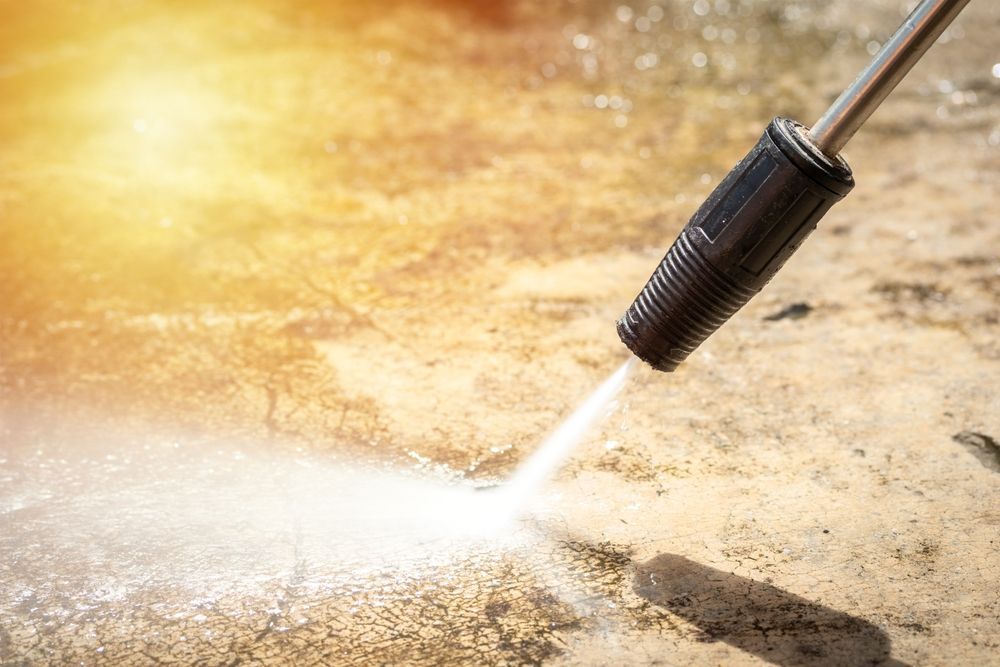 A pressure washer nozzle sprays a high-pressure jet of water onto a dirty surface, cleaning away grime.