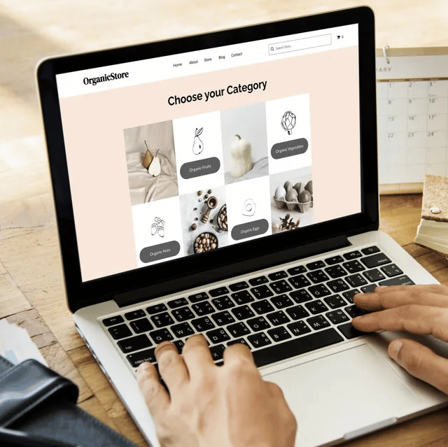 Person using laptop showing a website with product categories on a wooden desk.