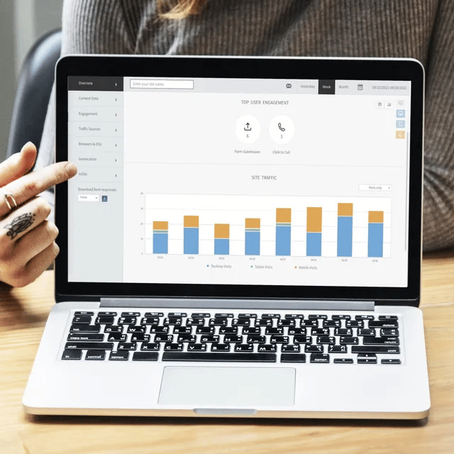 Person pointing at a laptop screen displaying a bar graph, with blue and orange bars, possibly analytics data.