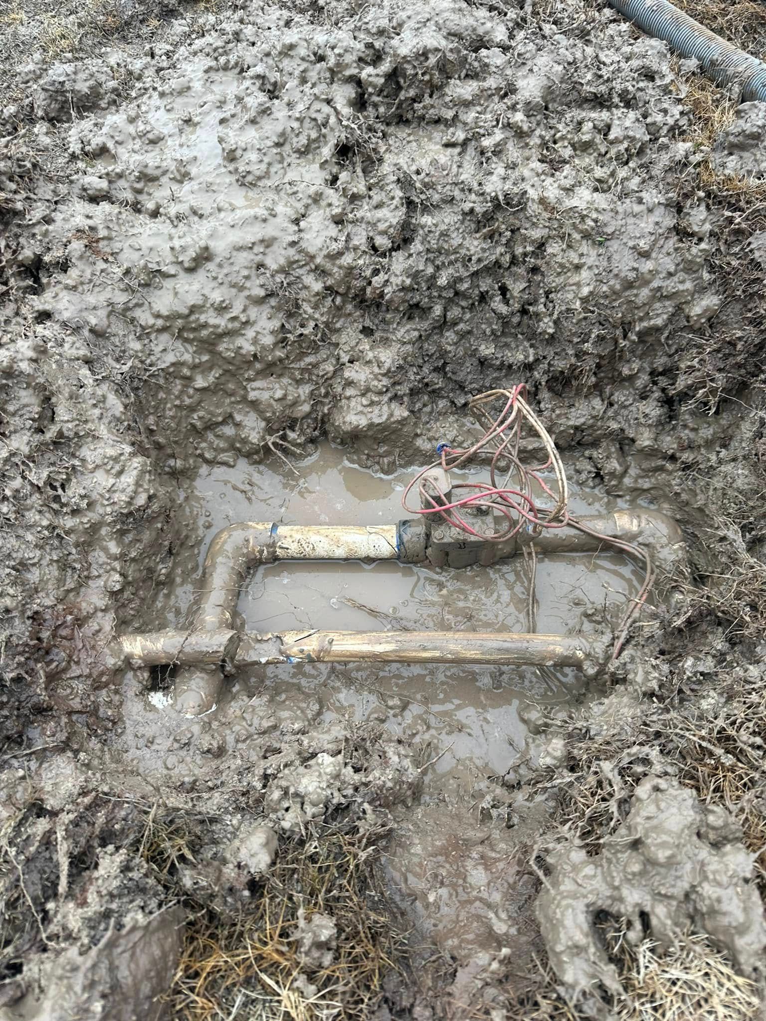 Pipes in muddy ground, possibly a water valve. Wet, brown mud surrounds the metal.