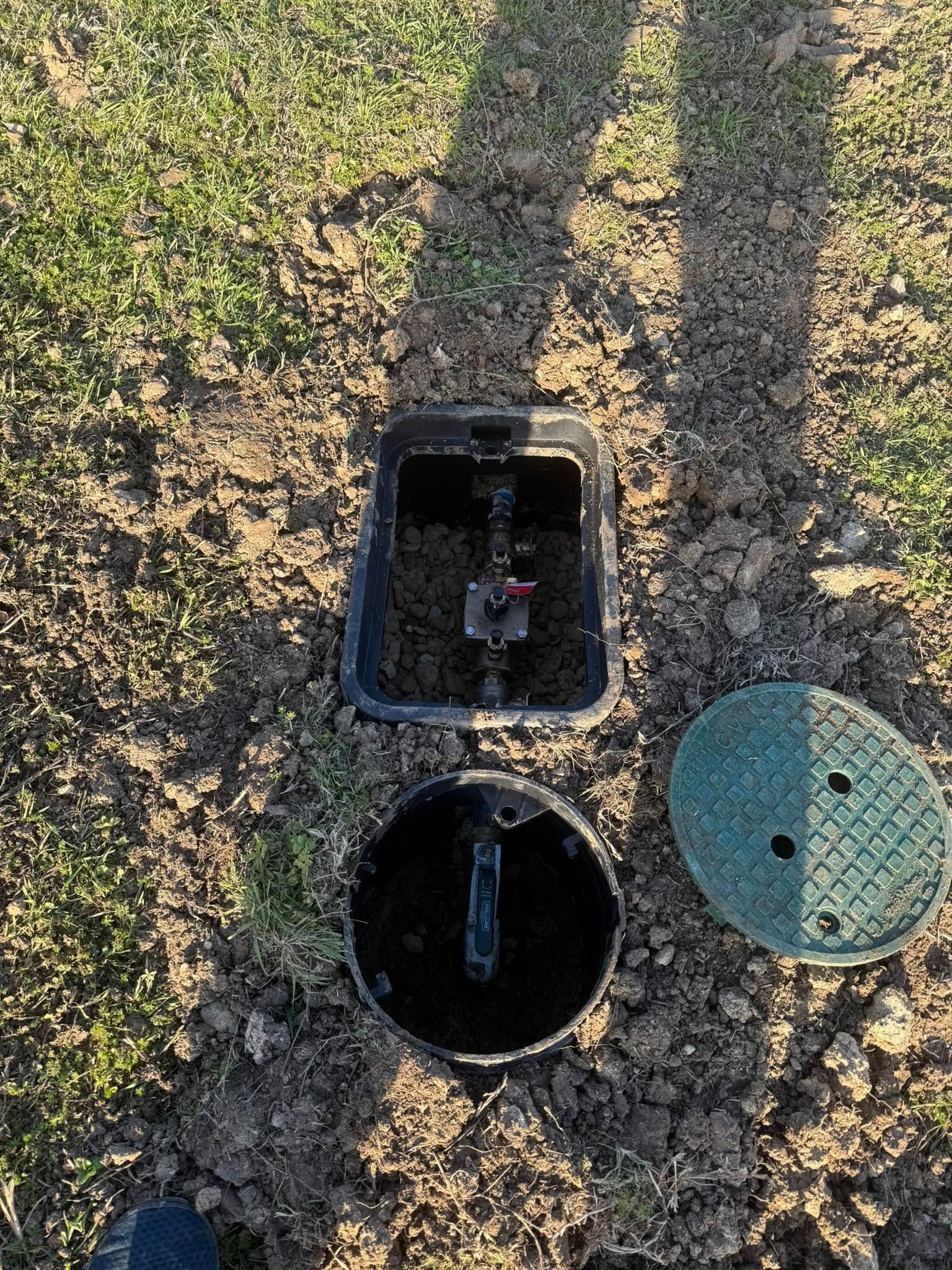 Open irrigation valve box in a grassy yard, with lid and valve visible.