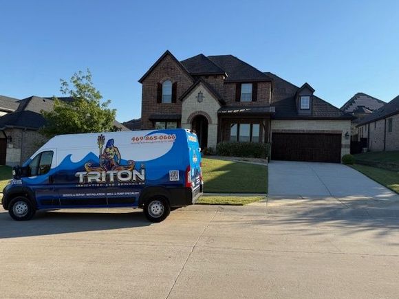 Blue and white Triton service van parked in front of a two-story brick home on a sunny day.