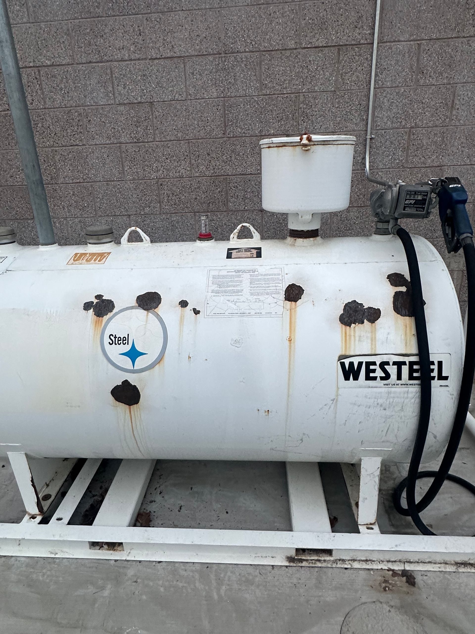 White Westeel fuel storage tank with rust spots, dispenser nozzle, and fill spout.