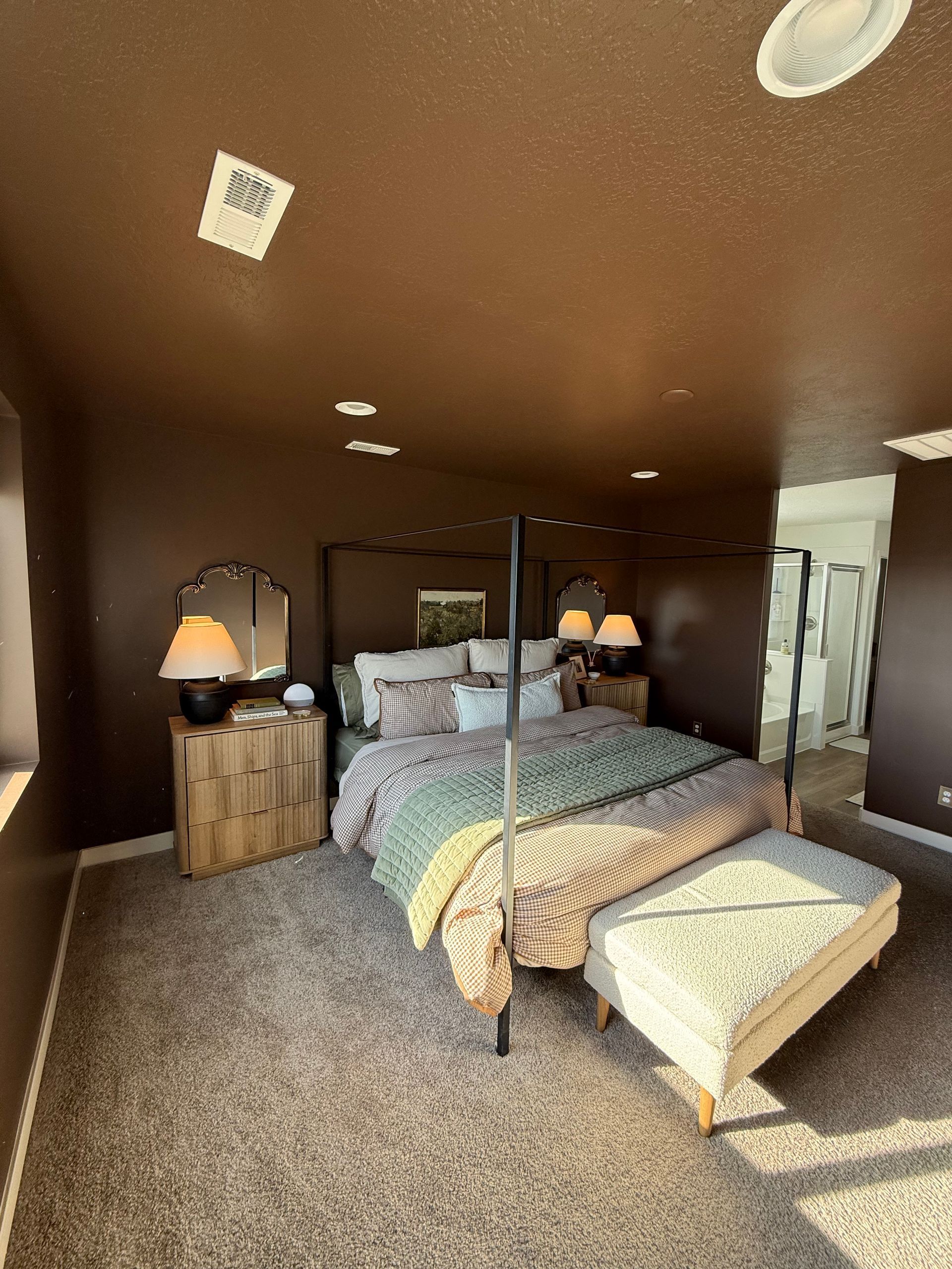 Bedroom with brown walls, four-poster bed, nightstands, rug, and an ottoman at the foot of the bed.