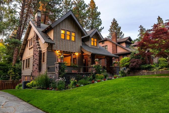 A cozy, two-story Craftsman home with glowing windows and a lush green lawn.