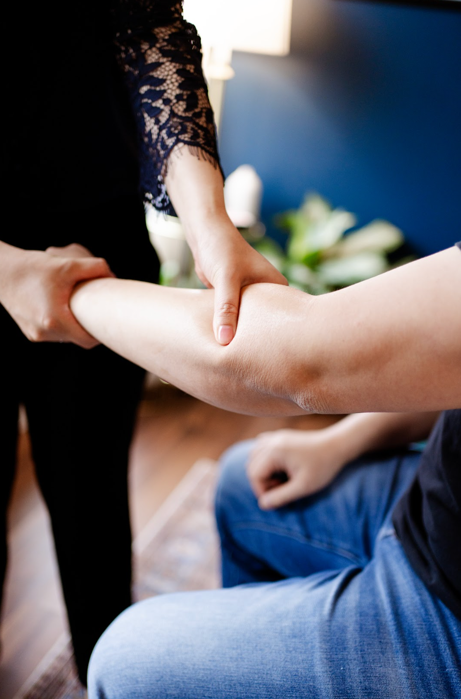 Person holding another person's forearm during a massage session, with blue jeans visible.
