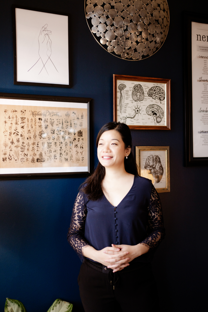 Woman standing in a dark gallery with framed art and wall decor behind her