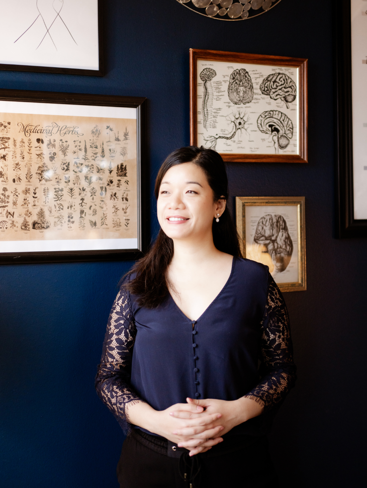 Woman standing in a dark gallery with framed art and wall decor behind her