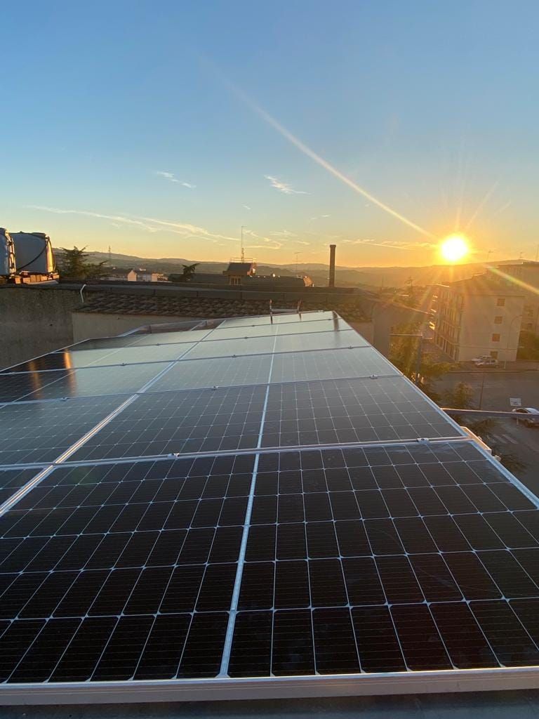 Una fila di pannelli solari sul tetto di un edificio al tramonto.