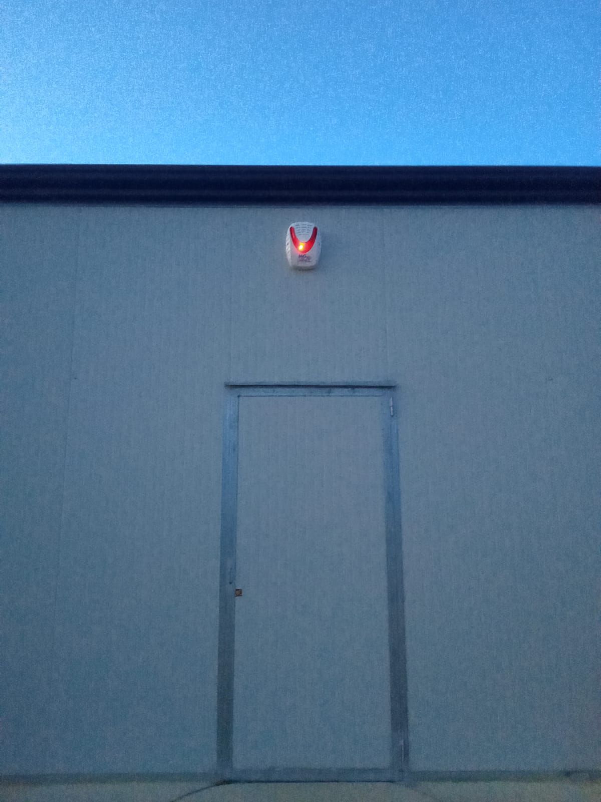 Un edificio grigio con una porta e un allarme rosso sul tetto